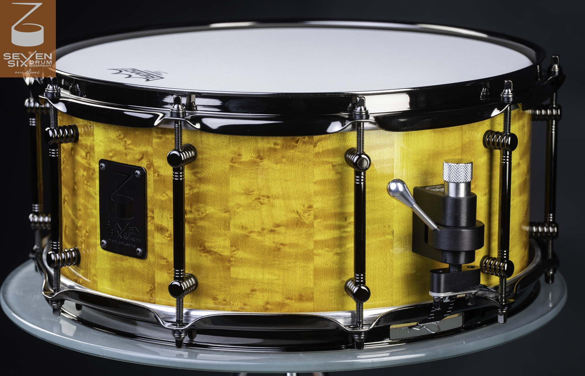 Handmade snare drum with a glossy yellow figured maple shell, black nickel tube lugs, and a machined throw-off.