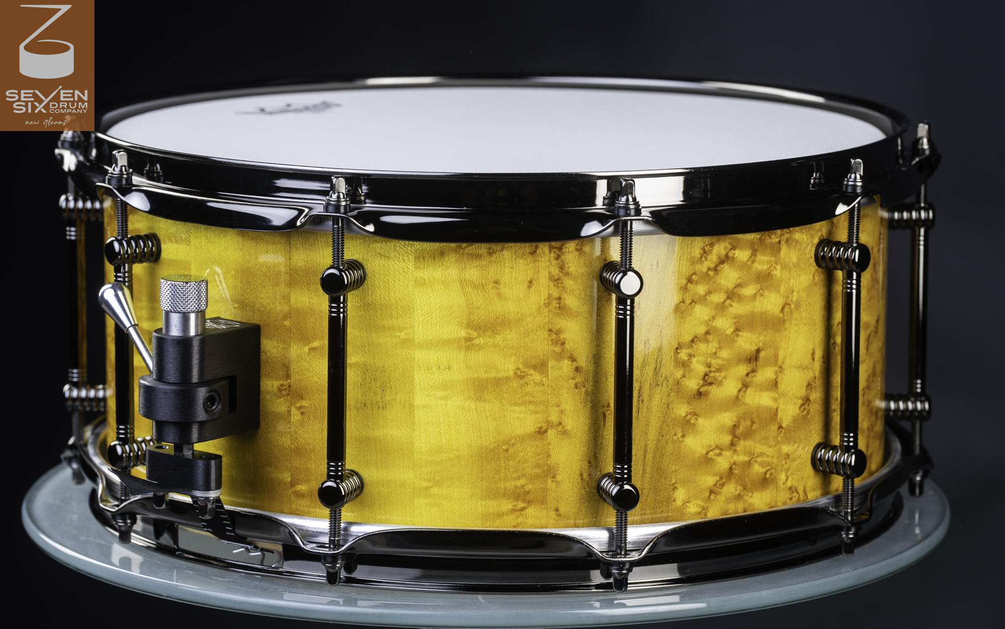 Handmade snare drum featuring a glossy amber birdseye maple shell, black nickel hoops, tube lugs, and an adjustable throw-off.