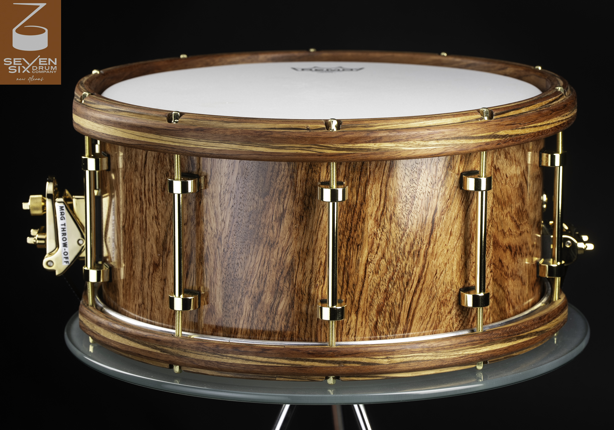 Handmade snare drum with a glossy natural wood shell, matching wooden hoops, and polished gold tube lugs and throw-off.