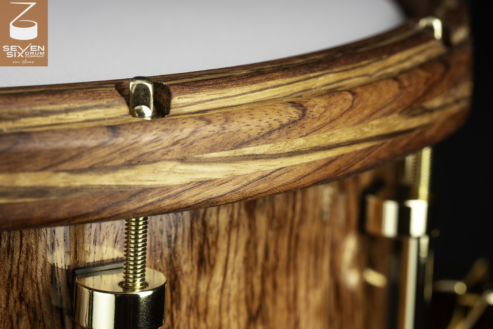Close-up of a snare drum with a glossy natural wood shell, matching contoured wood hoop, and polished brass hardware.