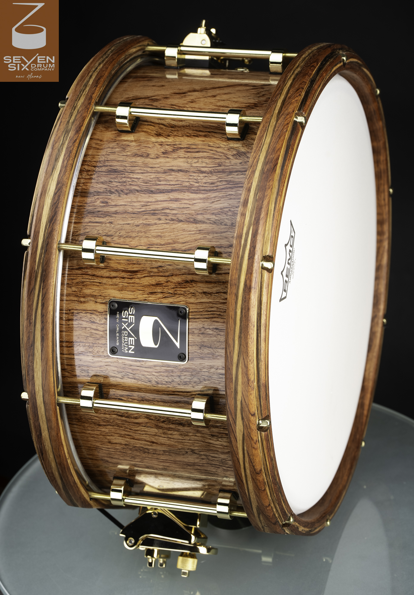 Glossy natural wood snare drum with matching wooden hoops, brass tube lugs, and gold hardware.