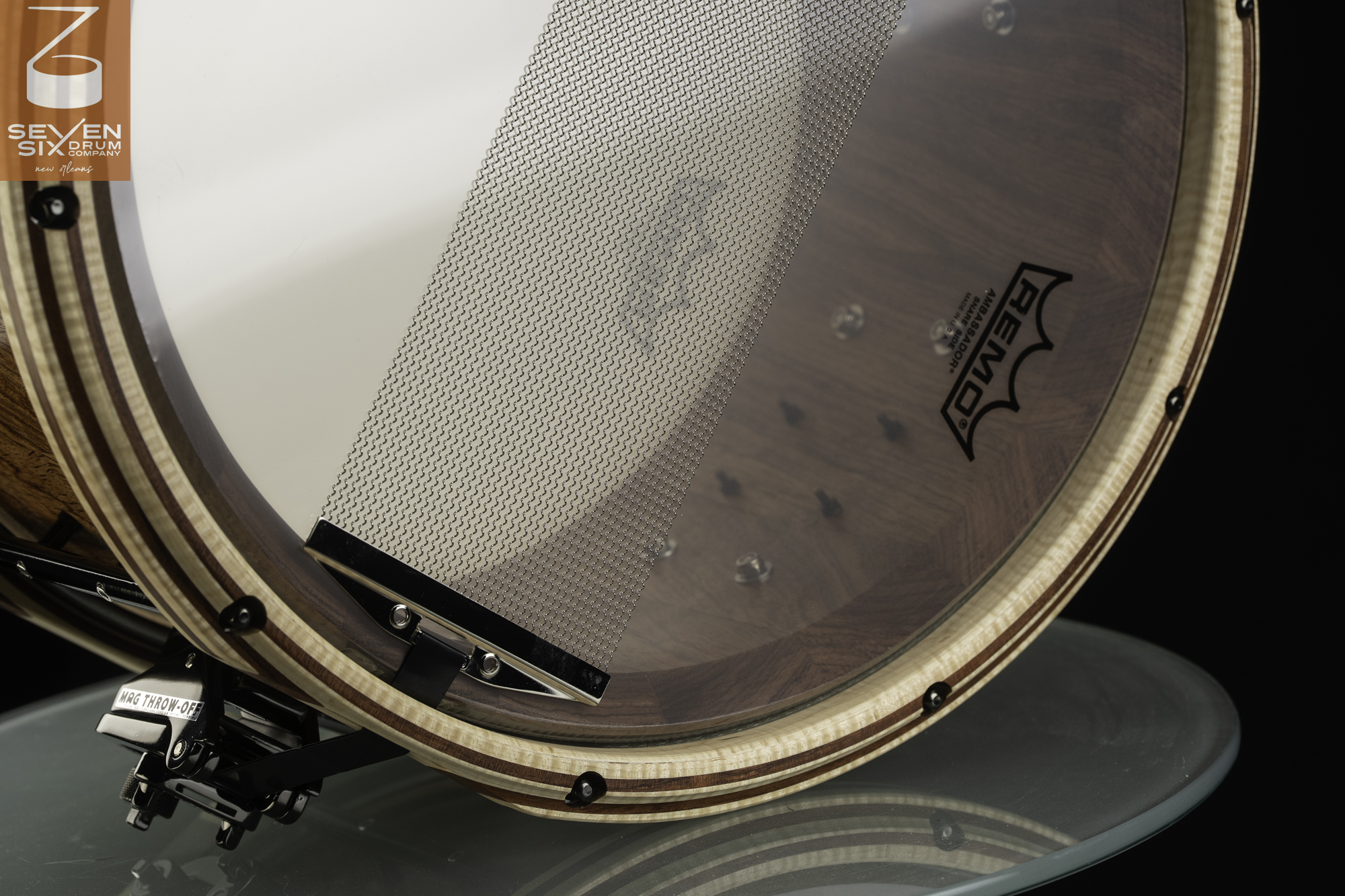 Bottom of a custom snare drum featuring a flamed maple hoop with dark inlay, steel snare wires, and a black MAG throw-off mechanism.