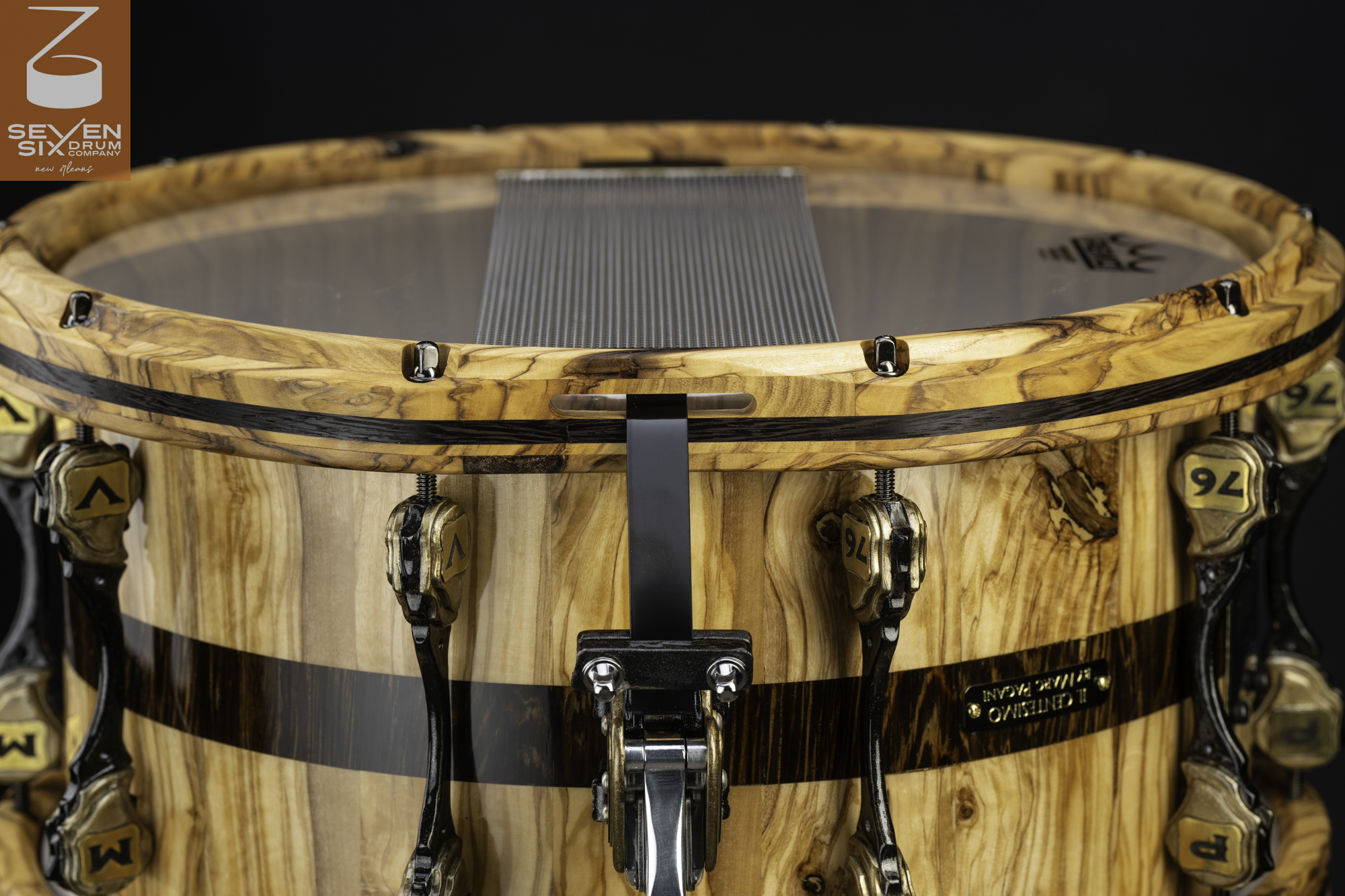 Natural wood snare drum with dark inlays, gloss finish, matching wood hoops, brass-accented lugs, and a metal snare strainer.