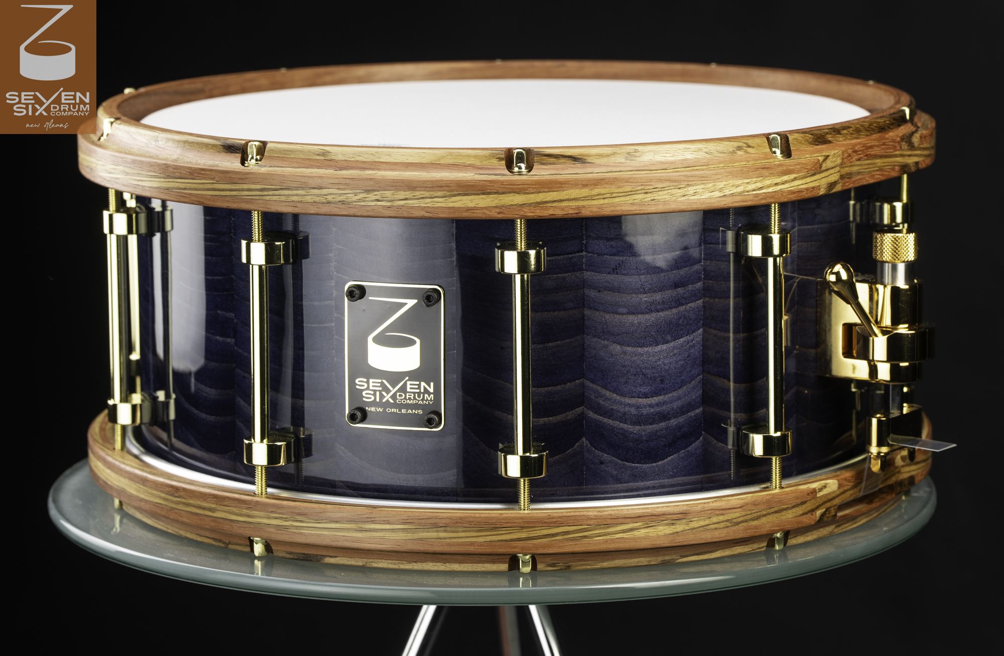 Handmade snare drum with a glossy blue figured Louisiana sinker Cypress wood shell, natural striped Bubinga nad Zebrawood hoops, and polished brass hardware.