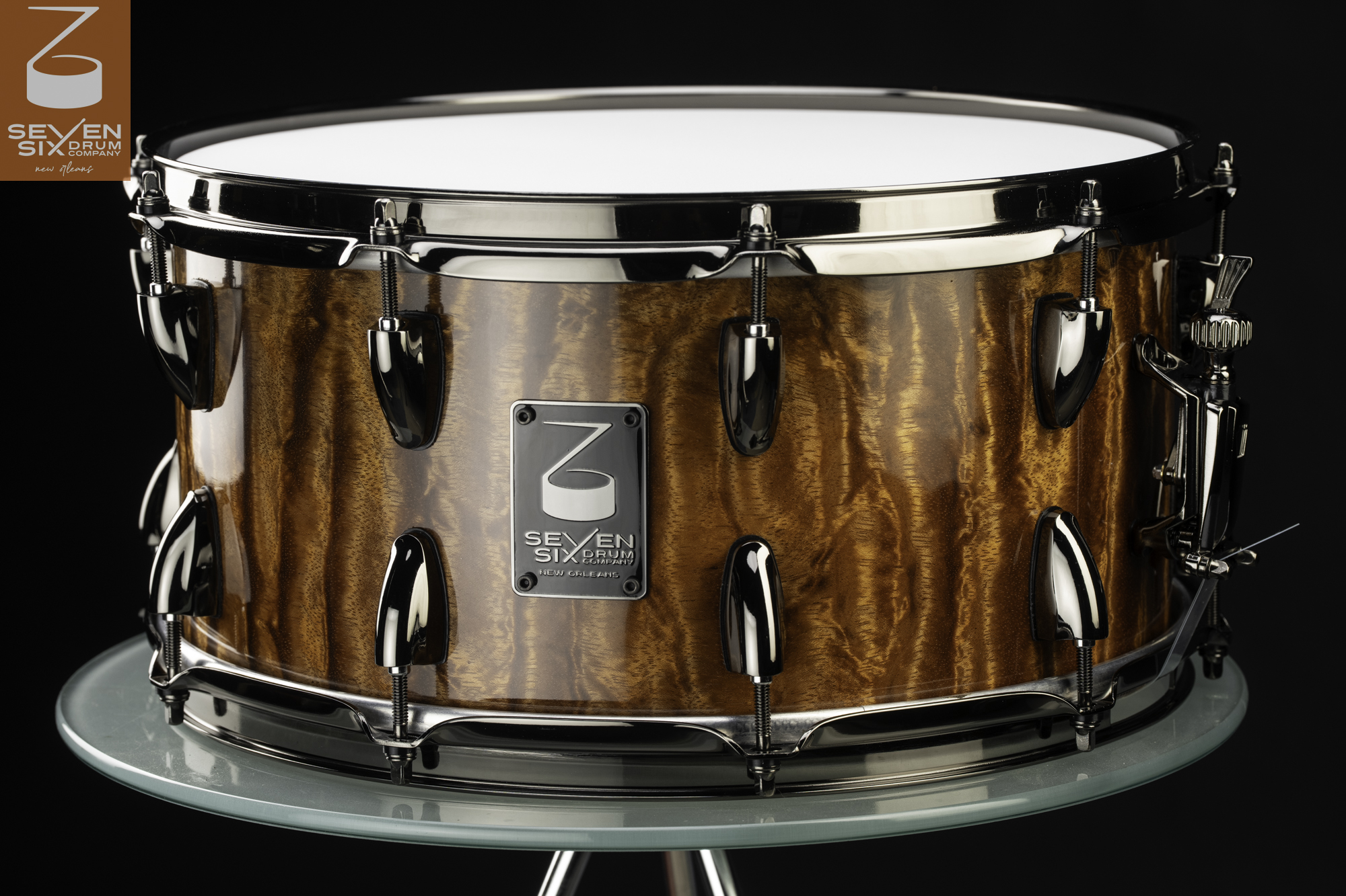 Handmade snare drum featuring a glossy figured waterfall Bubinga wood shell with black nickel hoops and teardrop lugs.