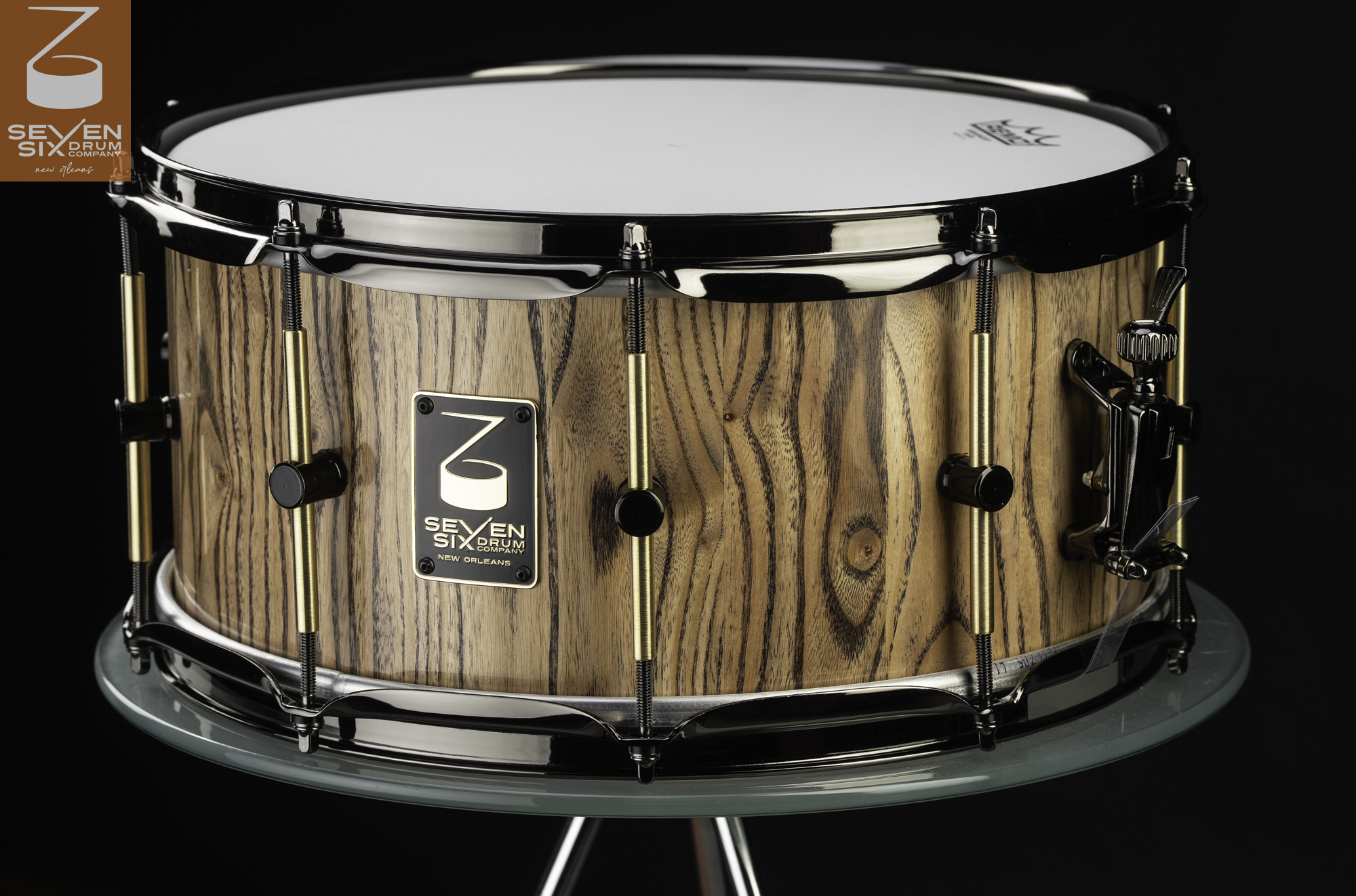 Handmade Chinaberry snare drum with a natural dark-grained wood, glossy black hoops, and brass tube lugs.