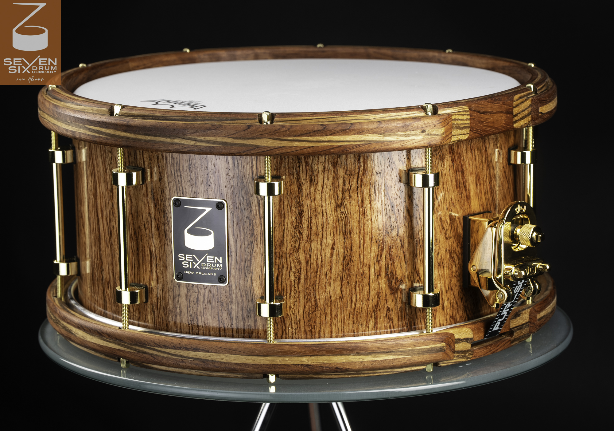 Gloss-finished wood Bubinga snare drum featuring matching Bubinga and Zebrawood wooden hoops, polished gold tube lugs, and a gold throw-off.